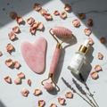 Rose quartz gua sha tool and facial roller on white marble with rose petals